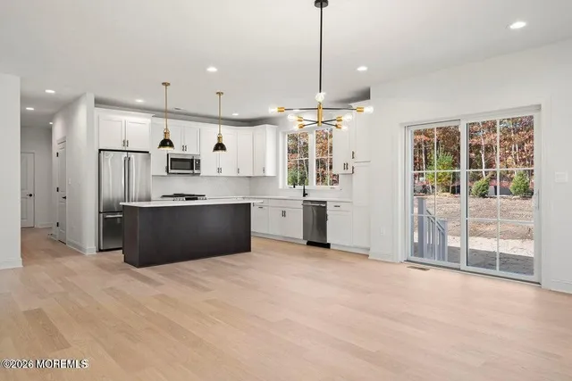 a large kitchen with stainless steel appliances kitchen island a stove a refrigerator a sink dishwasher a oven with white cabinets and wooden floor