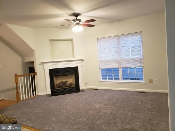 a view of a livingroom with a fireplace a ceiling fan and windows