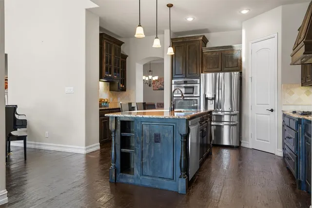 a kitchen with stainless steel appliances granite countertop a refrigerator a oven a stove and a wooden floors