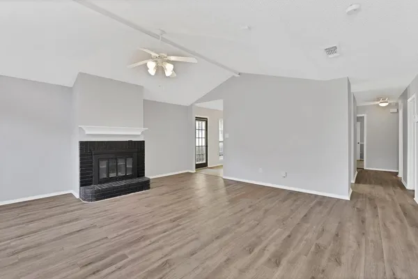 a view of an empty room with wooden floor fireplace and a window