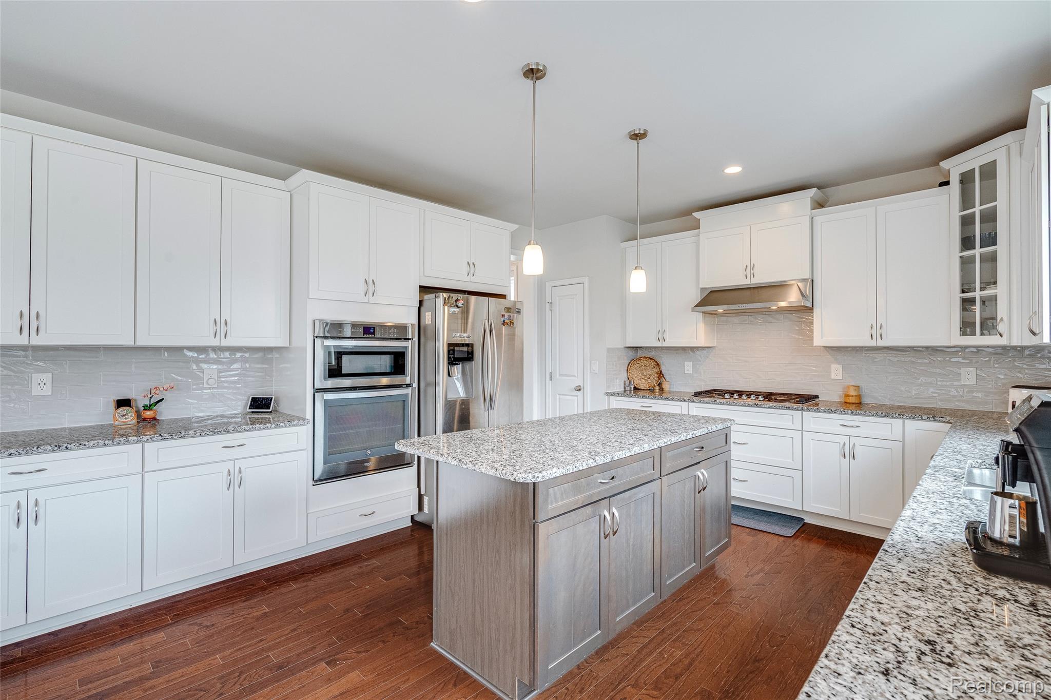 51011 Rockingham Drive Canton, MI 48188 - Photo 14 of 74 Two tone kitchen featuring light stone countertops, decorative light fixtures, glass insert cabinets, a center island, and dark wood-style flooring