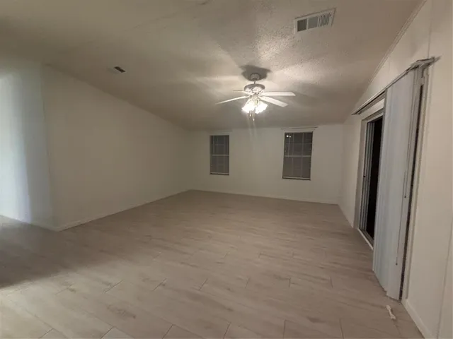 an empty room with chandelier fan and windows