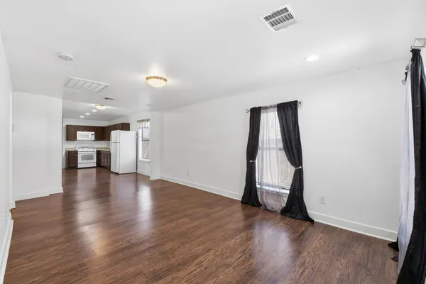 a view of empty room with wooden floor and kitchen