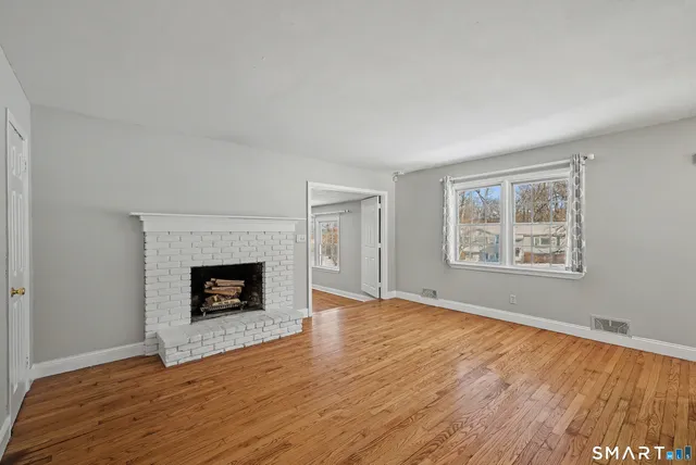 a view of an empty room with wooden floor fireplace and a window