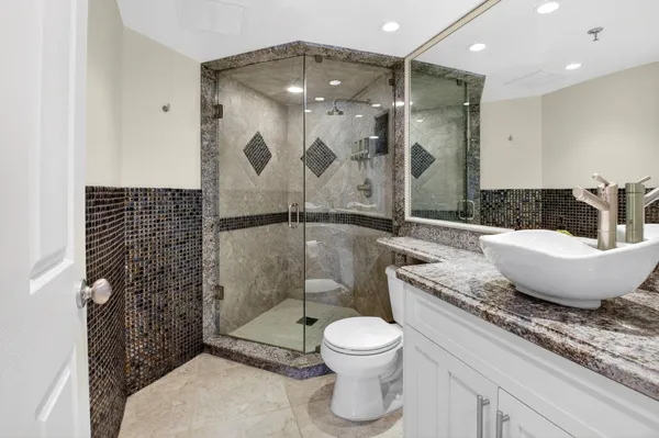 a bathroom with a granite countertop sink a toilet a mirror and shower