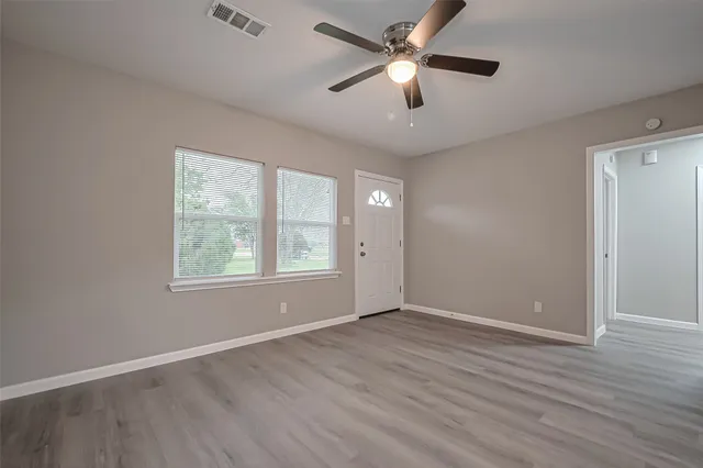 an empty room with wooden floor fan and windows