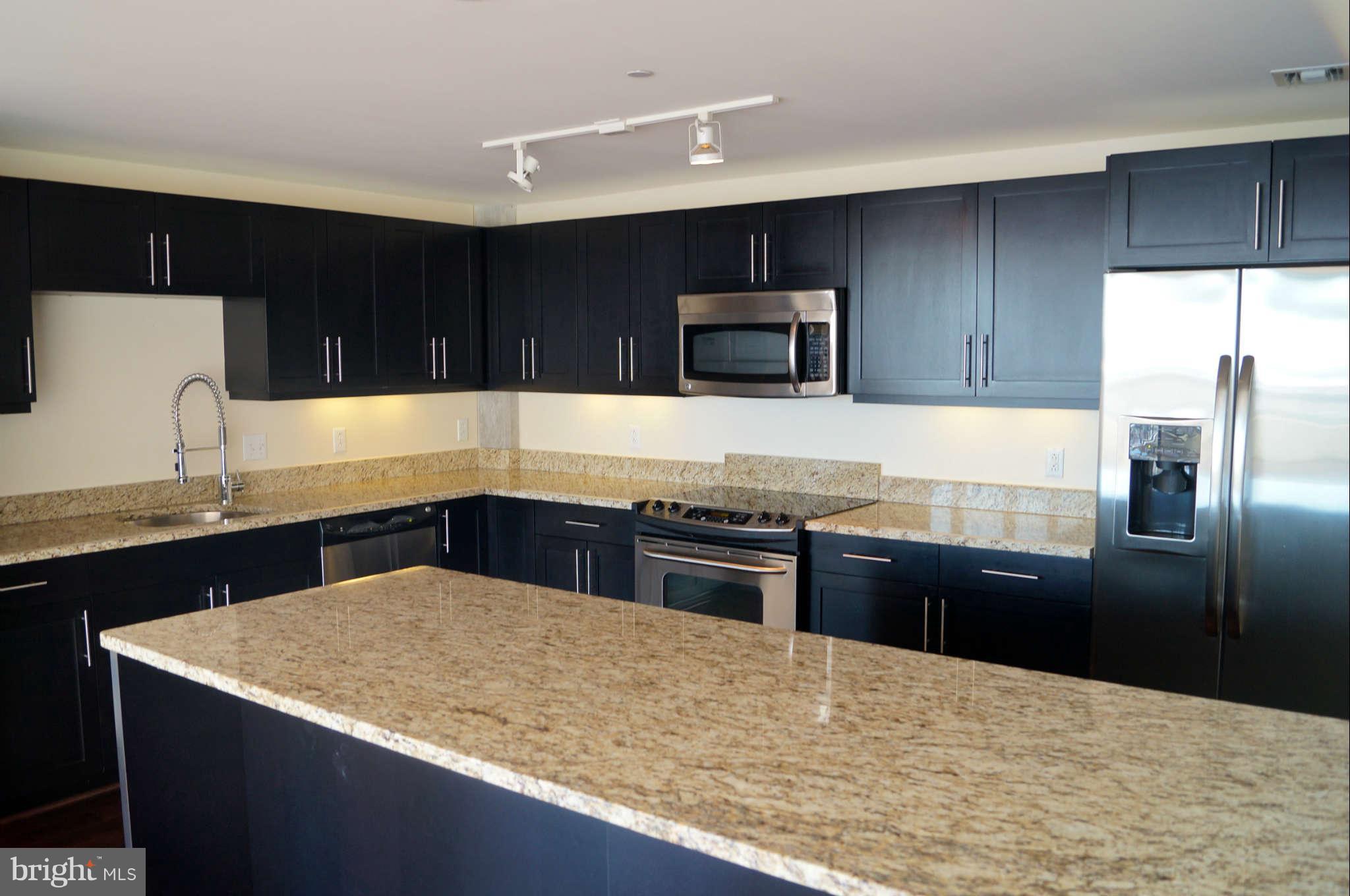 1200 Steuart Street, Unit 822 Baltimore, MD 21230 - Photo 11 of 30 a kitchen with granite countertop stainless steel appliances and wooden cabinets