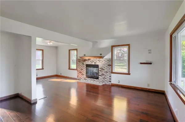 an empty room with wooden floor fireplace and windows
