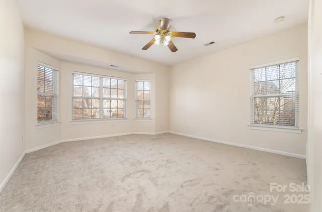 an empty room with chandelier fan and windows