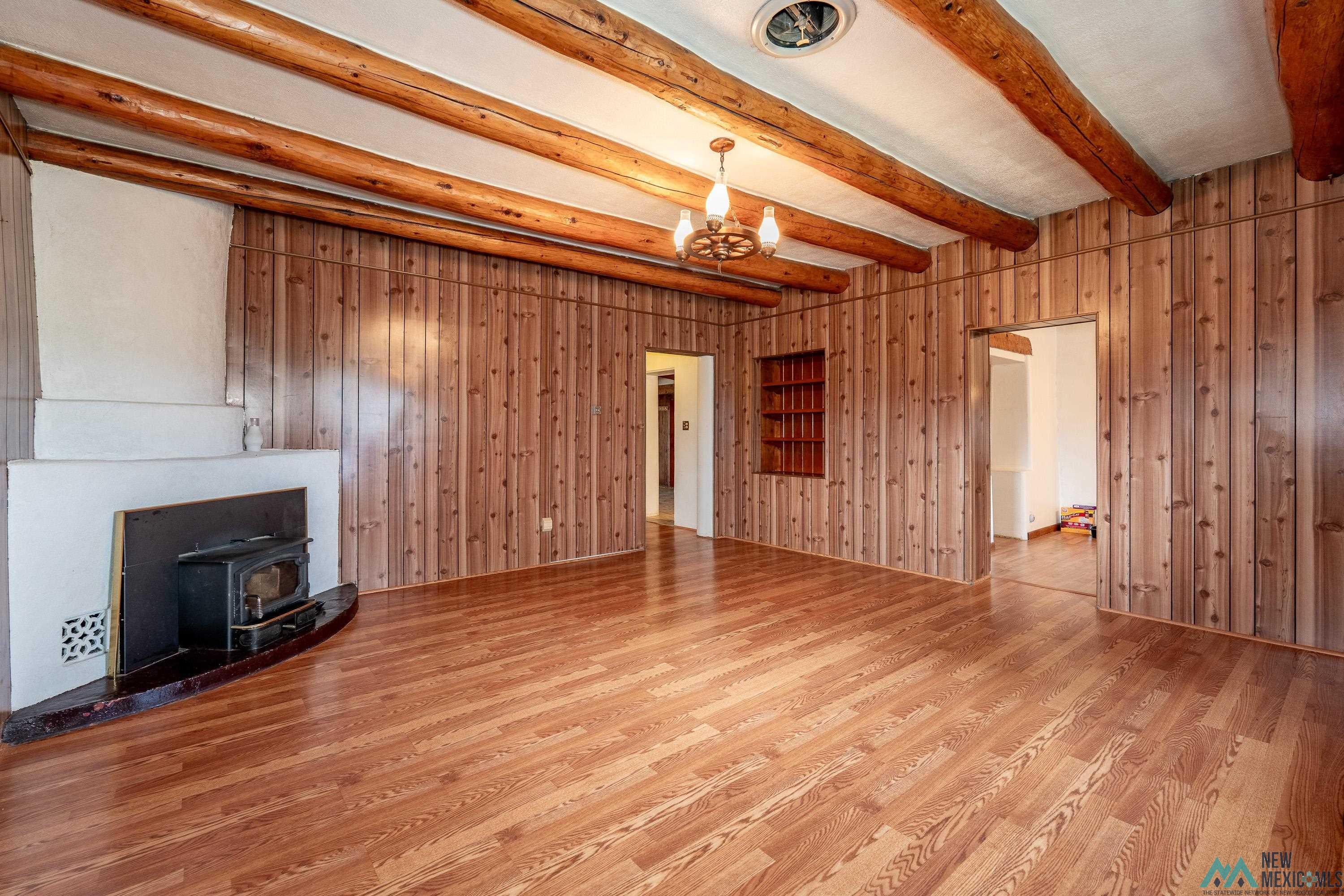 35234 Highway 87 Raton, NM 87740 - Photo 9 of 90 Unfurnished living room featuring a wood stove, wood walls, light wood-style flooring, beamed ceiling, and a chandelier