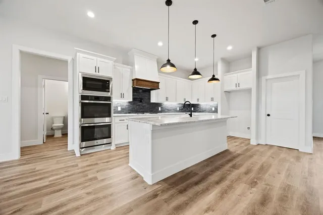 a large kitchen with white cabinets stainless steel appliances and wooden floor