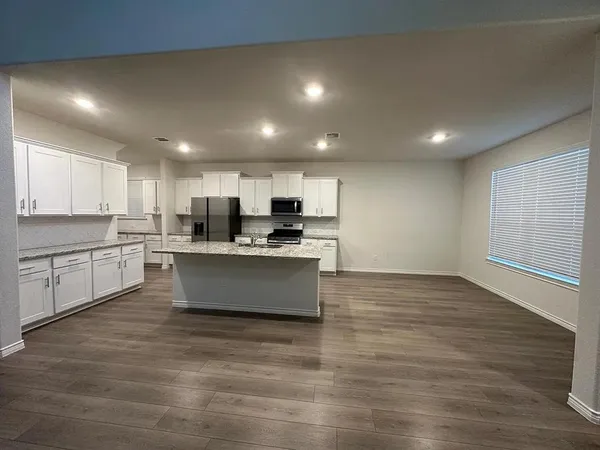 a large kitchen with stainless steel appliances granite countertop a stove a sink a refrigerator and white cabinets with wooden floor