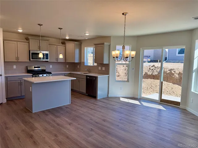 a kitchen with stainless steel appliances granite countertop a refrigerator a sink dishwasher a stove and a wooden floor