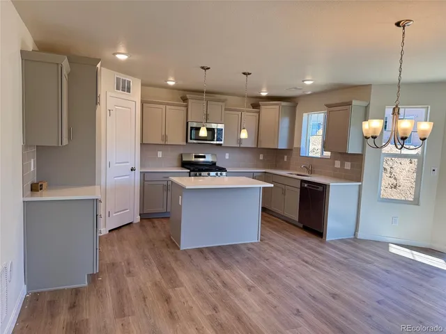 a large kitchen with stainless steel appliances granite countertop a stove a sink a refrigerator and white cabinets with wooden floor