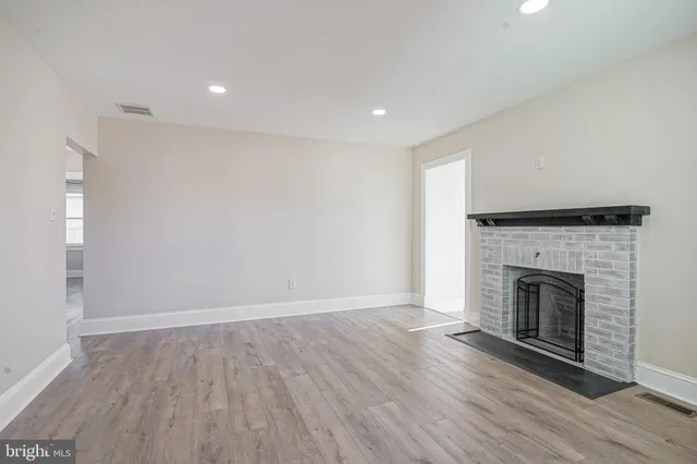 a view of an empty room with wooden floor fireplace and a window