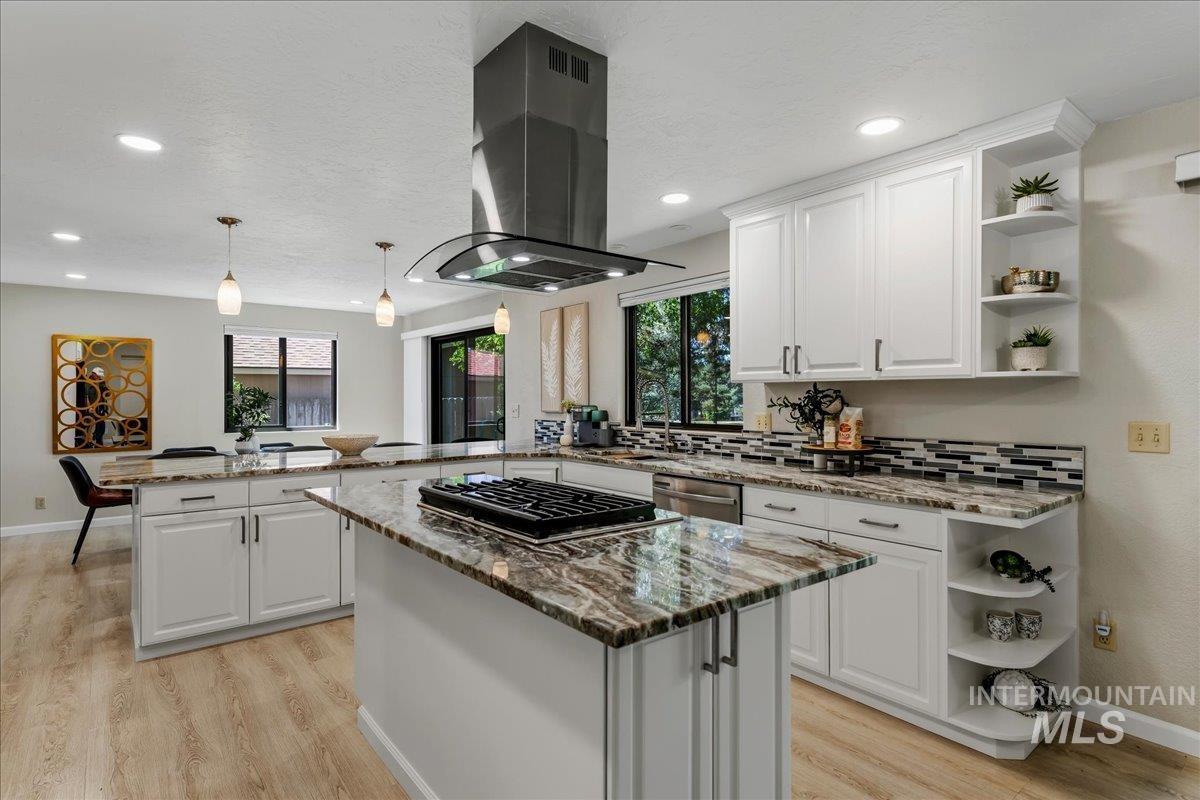 599 Pebble Beach Way Eagle, ID 83616 - Photo 11 of 44 Open-concept kitchen featuring an island with a built-in gas cooktop, a stainless steel range hood, stone countertops, white shaker cabinetry, and wood-finish flooring