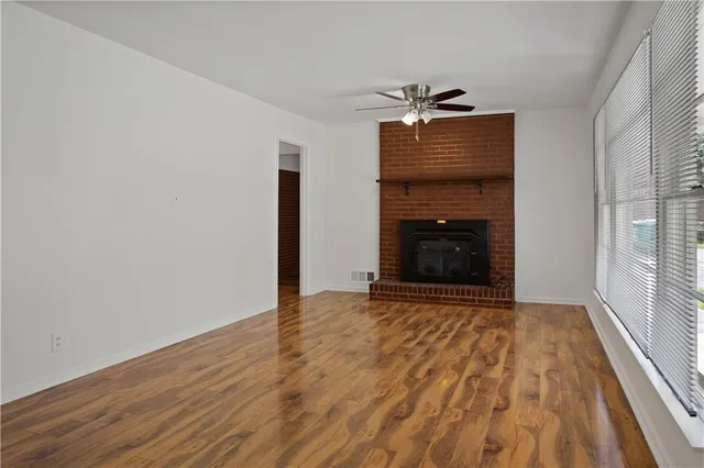 a view of an empty room with wooden floor fireplace and a window
