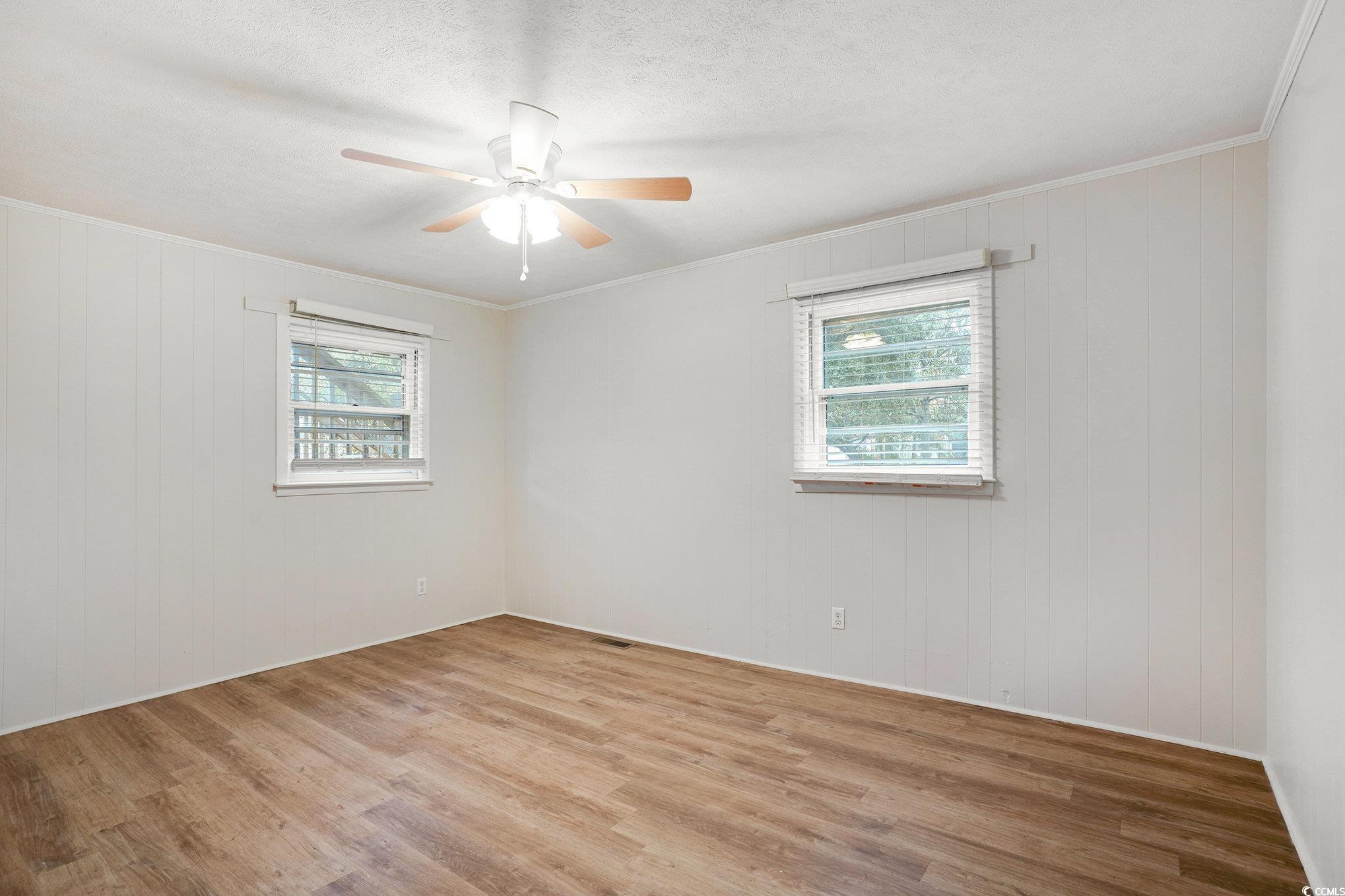 603 Maple Street Myrtle Beach, SC 29577 - Photo 11 of 40 Empty room featuring light wood-style floors, healthy amount of natural light, crown molding, wood walls, and a ceiling fan