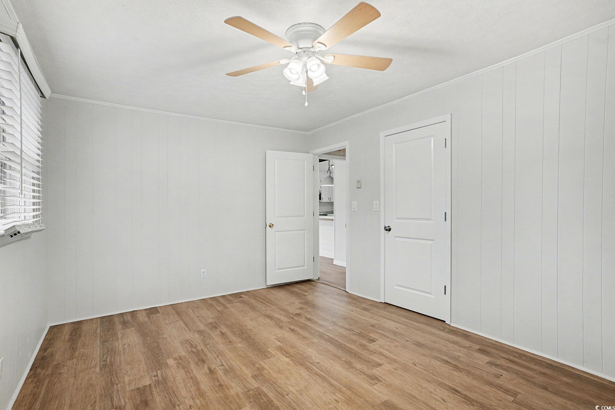 603 Maple Street Myrtle Beach, SC 29577 - Photo 12 of 40 Empty room with crown molding, light wood-style floors, wooden walls, and a ceiling fan