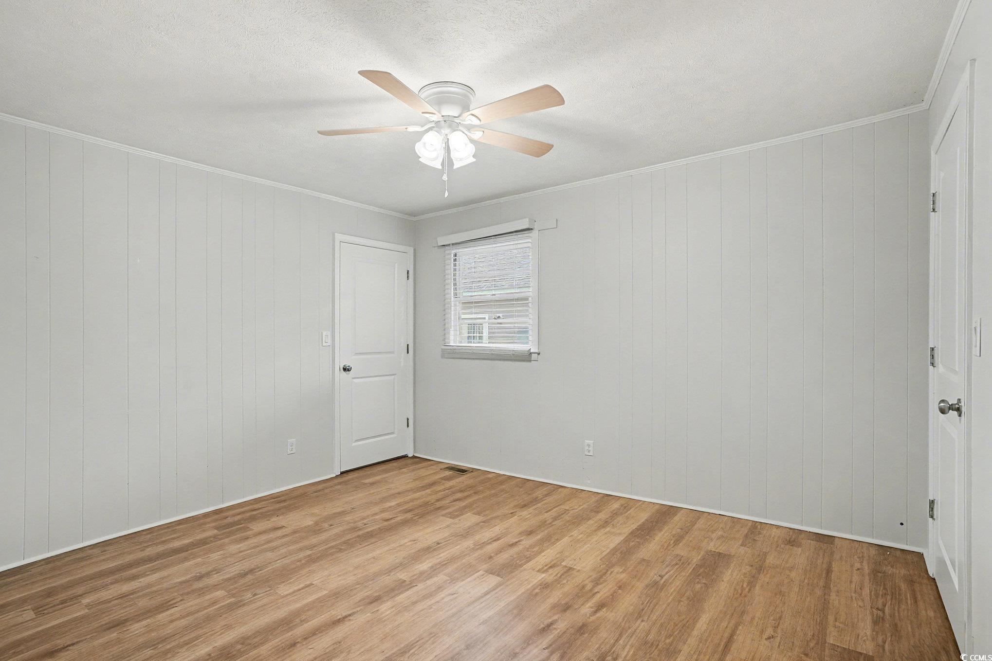 603 Maple Street Myrtle Beach, SC 29577 - Photo 13 of 40 Spare room featuring light wood-style floors, ornamental molding, wooden walls, a ceiling fan, and a textured ceiling