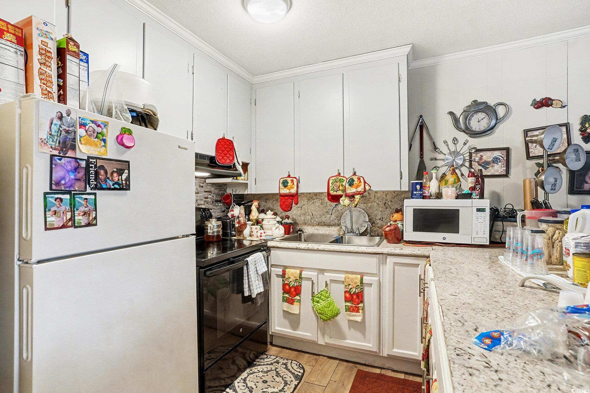 603 Maple Street Myrtle Beach, SC 29577 - Photo 30 of 40 Kitchen featuring white appliances, crown molding, white cabinets, under cabinet range hood, and light wood-style flooring
