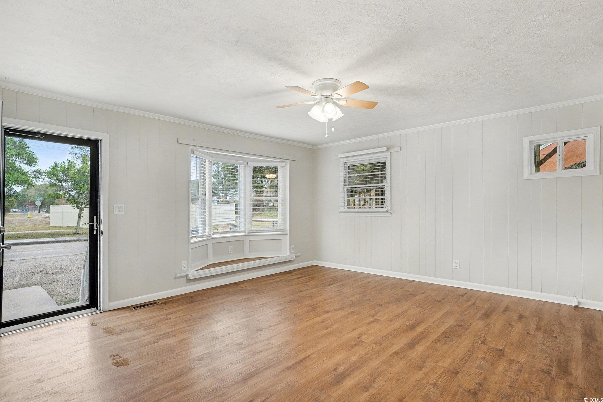 603 Maple Street Myrtle Beach, SC 29577 - Photo 4 of 40 Spare room featuring light wood-type flooring, ornamental molding, ceiling fan, and wooden walls
