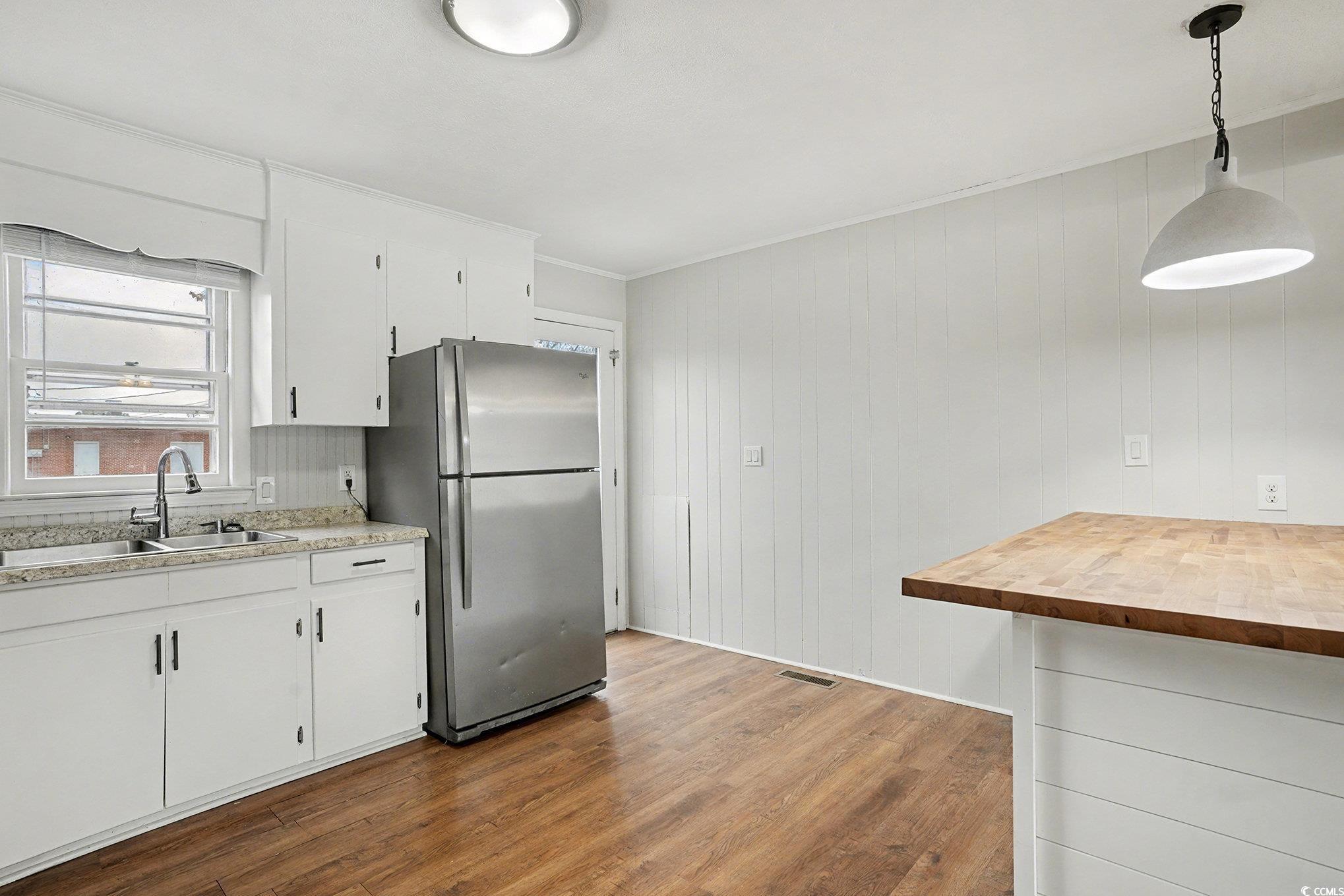 603 Maple Street Myrtle Beach, SC 29577 - Photo 8 of 40 Kitchen featuring freestanding refrigerator, light wood-style flooring, hanging light fixtures, white cabinets, and wooden walls