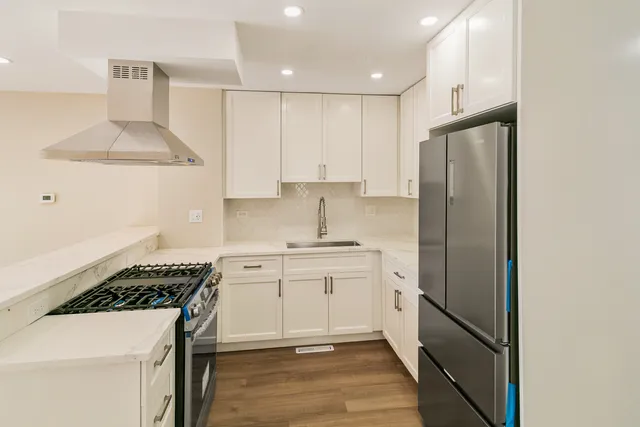 a kitchen with stainless steel appliances a refrigerator a sink and white cabinets