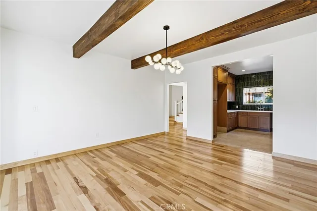 a view of an empty room with wooden floor and a kitchen