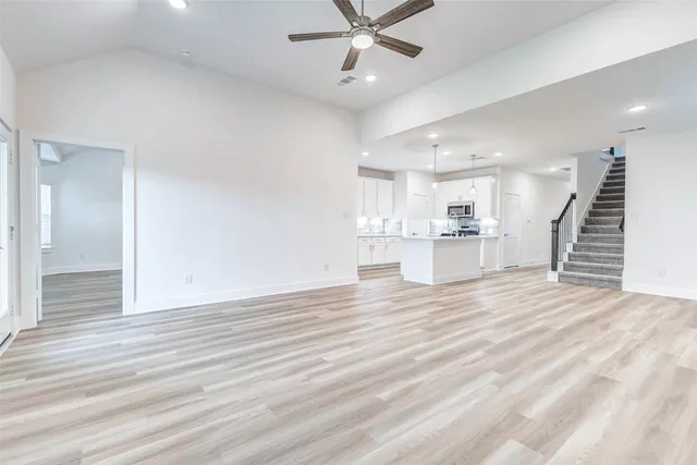 an empty room with wooden floor and kitchen view