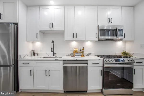a kitchen with stainless steel appliances granite countertop a stove a sink and a refrigerator with white cabinets