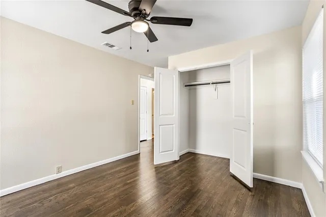 an empty room with wooden floor ceiling fan and windows