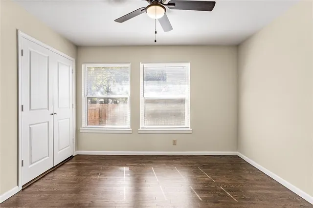 an empty room with wooden floor chandelier fan and windows