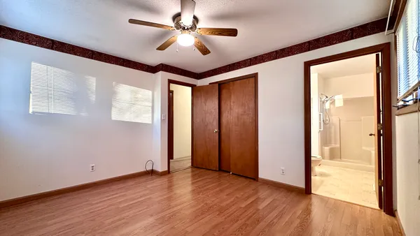 an empty room with wooden floor fan and windows