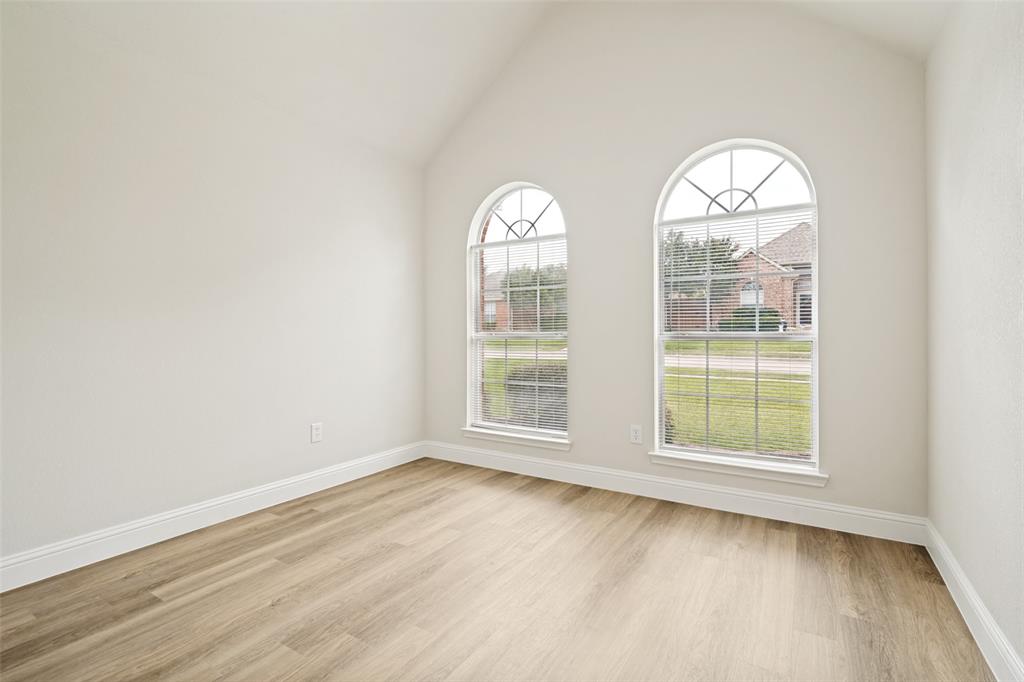 3020 Ridge Hollow Drive Plano, TX 75023 - Photo 13 of 28 Room featuring two arched windows with internal grilles, wood-finish flooring, white baseboards, and vaulted ceilings