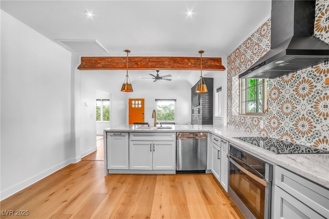 1318 Denver Street Boulder City, NV 89005 - Photo 11 of 32 Kitchen featuring wall chimney range hood, hanging light fixtures, light stone counters, stainless steel appliances, and plenty of natural light