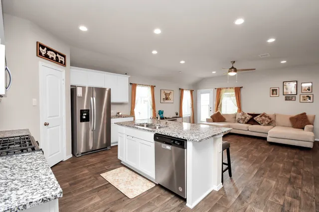 a kitchen with stainless steel appliances granite countertop a refrigerator a sink dishwasher a stove and white countertops with wooden floor