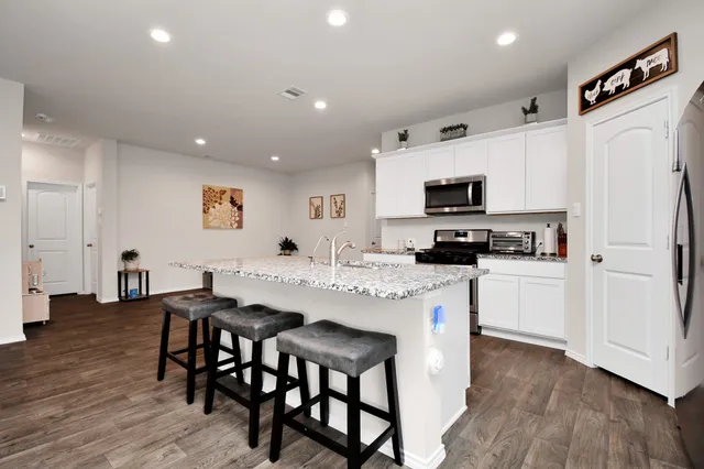 a kitchen with stainless steel appliances granite countertop a stove a sink a microwave a refrigerator and white cabinets with wooden floor