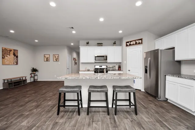 a kitchen with stainless steel appliances granite countertop a refrigerator a stove a sink a dining table and chairs with wooden floor