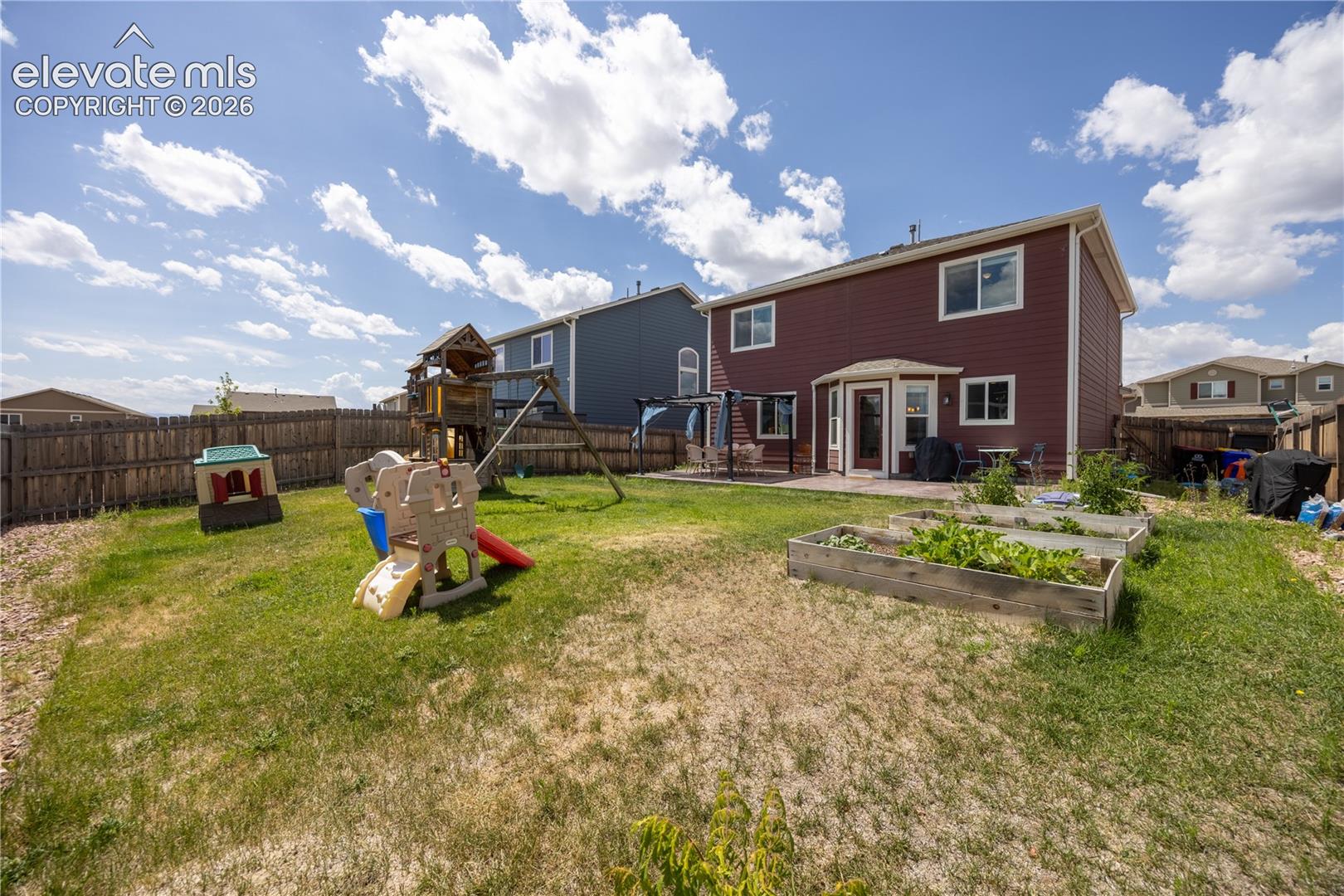 10993 Avena Road Peyton, CO 80831 - Photo 32 of 42 Expansive backyard featuring a fenced perimeter, raised garden beds, a ground-level patio, and a bay window
