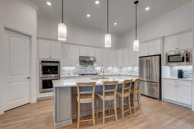 a kitchen with stainless steel appliances kitchen island granite countertop a refrigerator a stove microwave and white cabinets with wooden floor