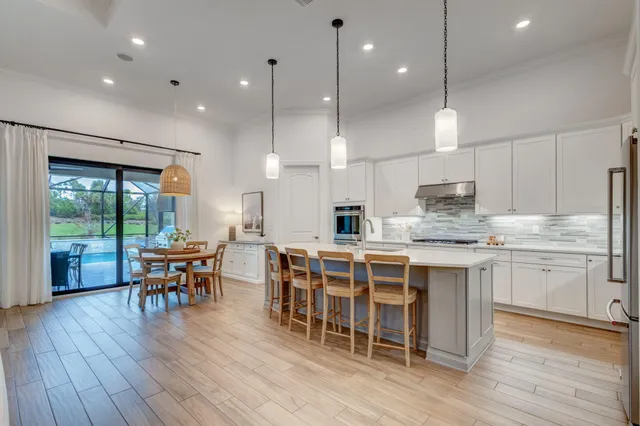 a kitchen with stainless steel appliances kitchen island granite countertop a stove a refrigerator a kitchen island a dining table and chairs with wooden floor
