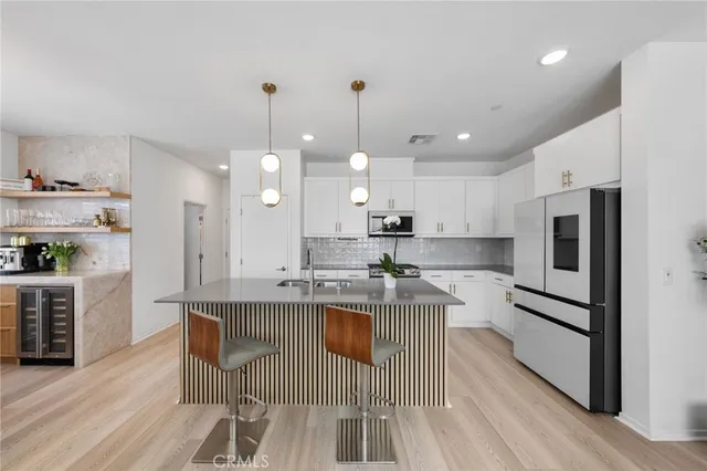 a very nice looking kitchen with granite countertop a stove a sink a refrigerator and a dining table with wooden floor