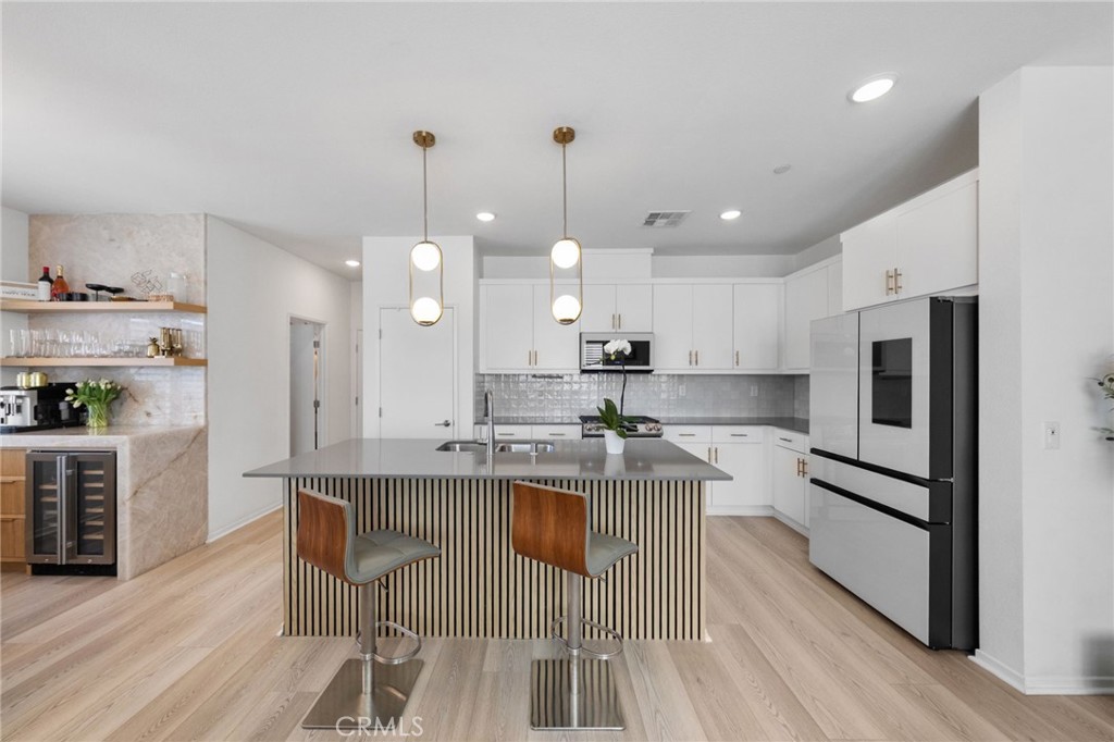 a very nice looking kitchen with granite countertop a stove a sink a refrigerator and a dining table with wooden floor