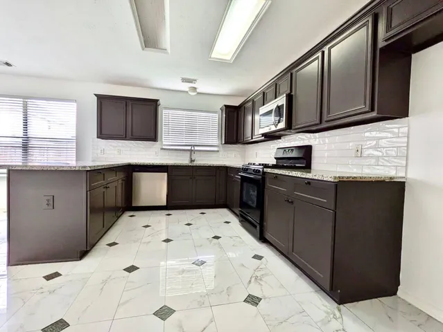 a kitchen with stainless steel appliances kitchen island granite countertop a sink a stove top oven and cabinets