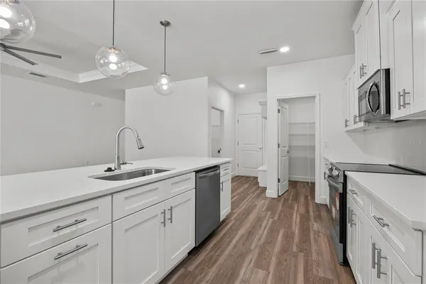 a kitchen with granite countertop a stove top oven a sink dishwasher and white cabinets with wooden floor