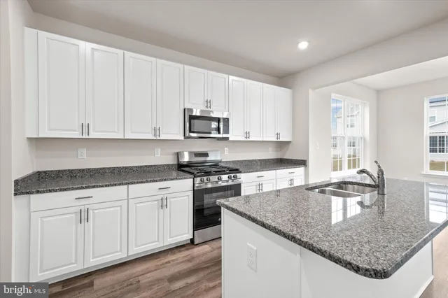 a kitchen with granite countertop a sink white cabinets and stainless steel appliances