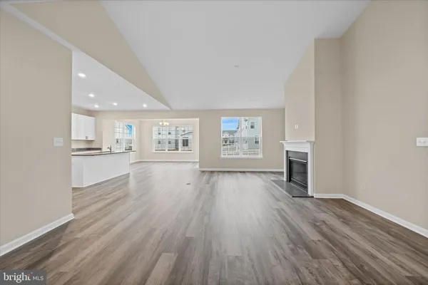 an empty room with wooden floor and kitchen view
