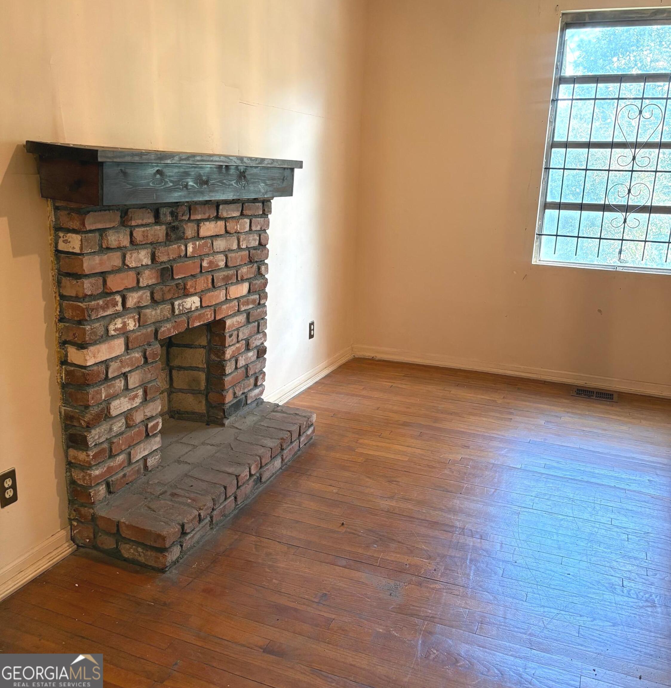 290 Florida Avenue Southwest Atlanta, GA 30310 - Photo 4 of 12 an empty room with wooden floor a fireplace and windows