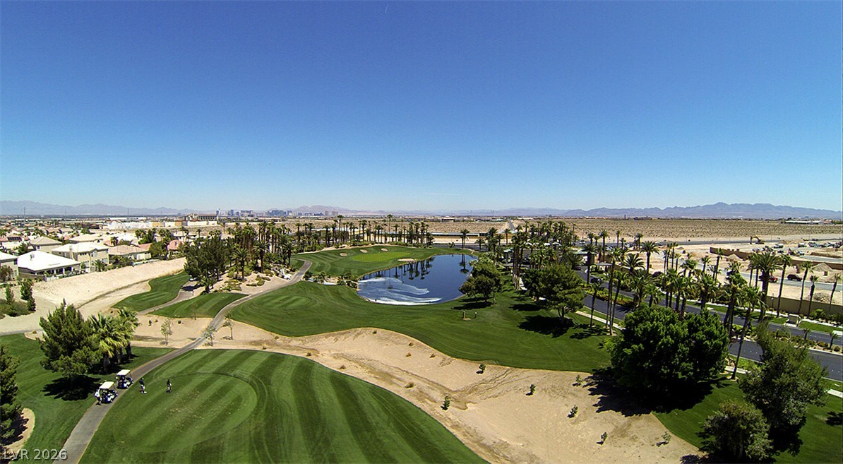 87 Tall Ruff Drive Las Vegas, NV 89148 - Photo 3 of 71 An aerial panorama reveals a verdant golf course winding through a desert landscape, bordered by residential homes and distant mountains.